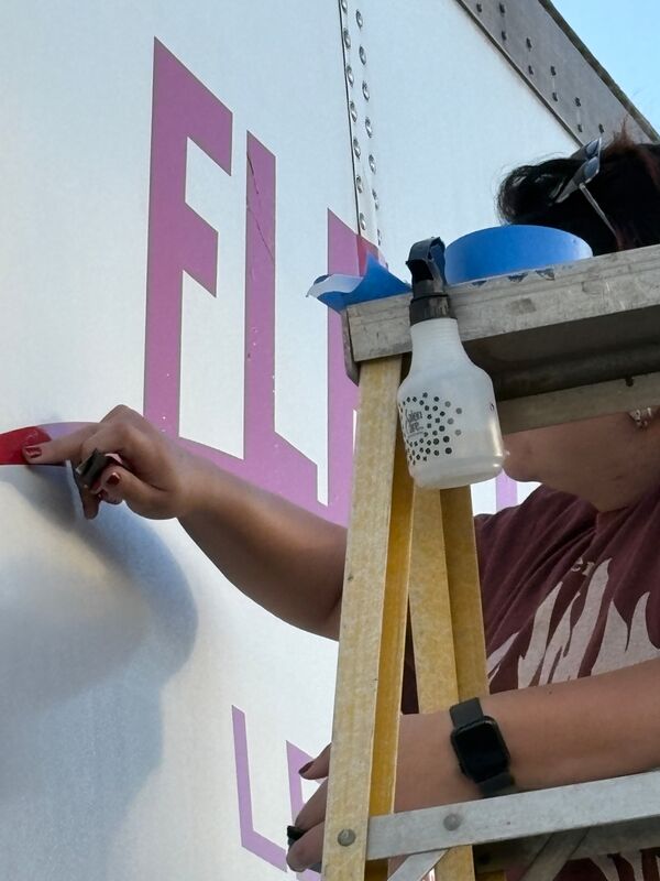 Close-up of vinyl lettering being squeegeed onto a trailer and the transfer tape peeled away