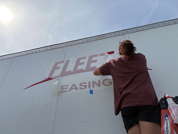 Installer positioning Fleet Leasing lettering on a trailer panel with transfer tape