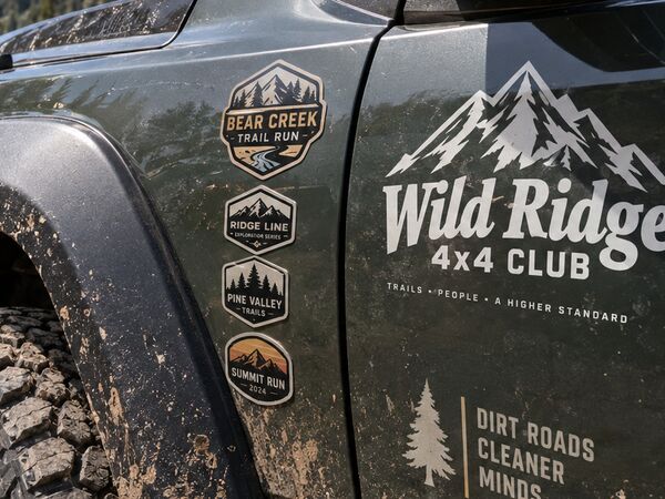 Trail-run badge decals and a 4x4 club logo on the fender and door of an off-road truck