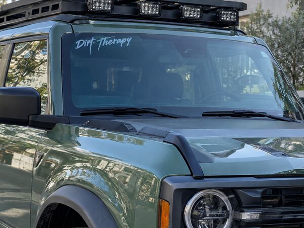 Green off-road SUV with a small single-color script visor decal on the windshield