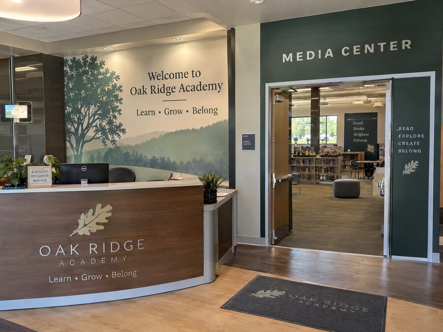 School entrance monument sign with a post-mounted wayfinding sign for main office, visitor parking, gym, and student drop-off